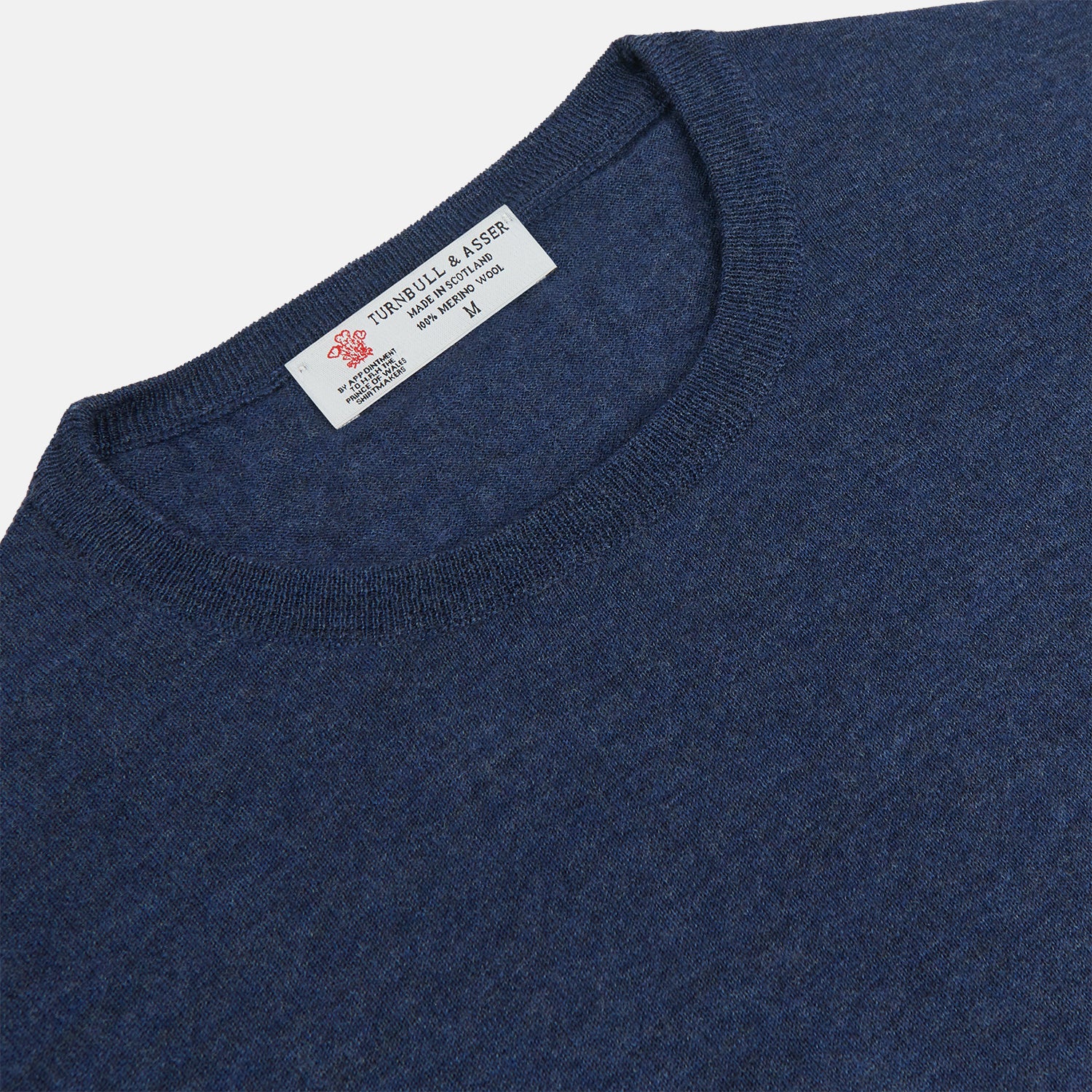 View 2 of product The Blue Crew Neck Merino Wool Jumper by Turnbull & Asser—a classic, long-sleeved staple with ribbed cuffs and hem—lies flat against a white background.