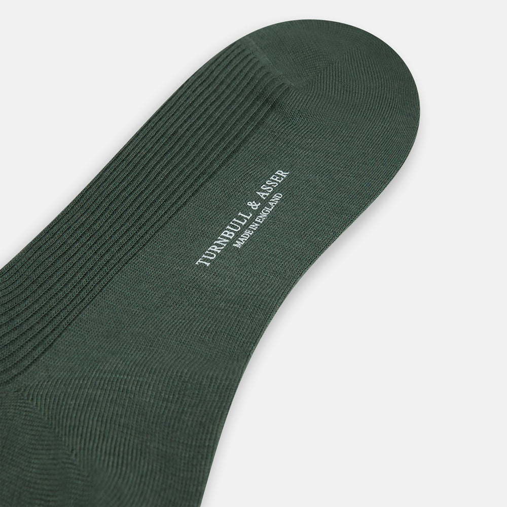 A single Fern Green Mid-Length Merino Sock by Turnbull & Asser, featuring a ribbed texture, is displayed on a plain white background at a slight angle to highlight its premium wool fabric, shape, and length.
