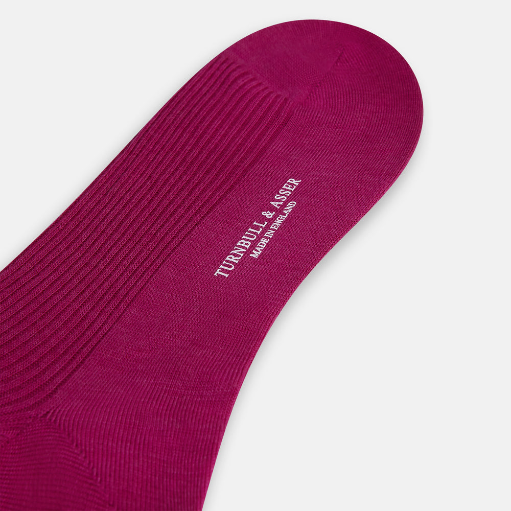 The Turnbull & Asser Magenta Mid-Length Merino Sock, featuring a ribbed design and crafted from soft merino wool, is displayed in a solid deep magenta color against a white background.