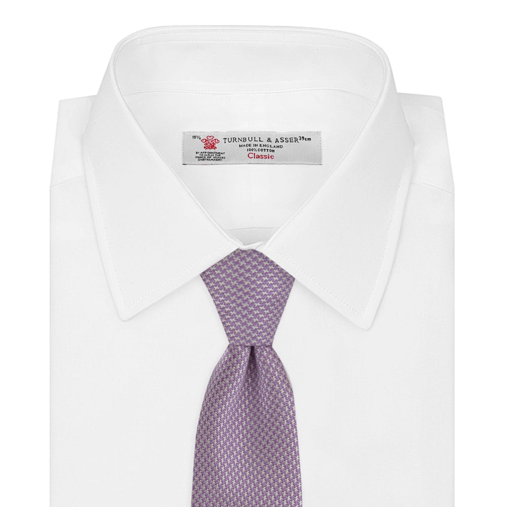 The Turnbull & Asser Lilac Houndstooth Silk Tie features a subtle houndstooth pattern and elegant silk weave—ideal for elevating your favorite office shirt. Displayed rolled on a white background.