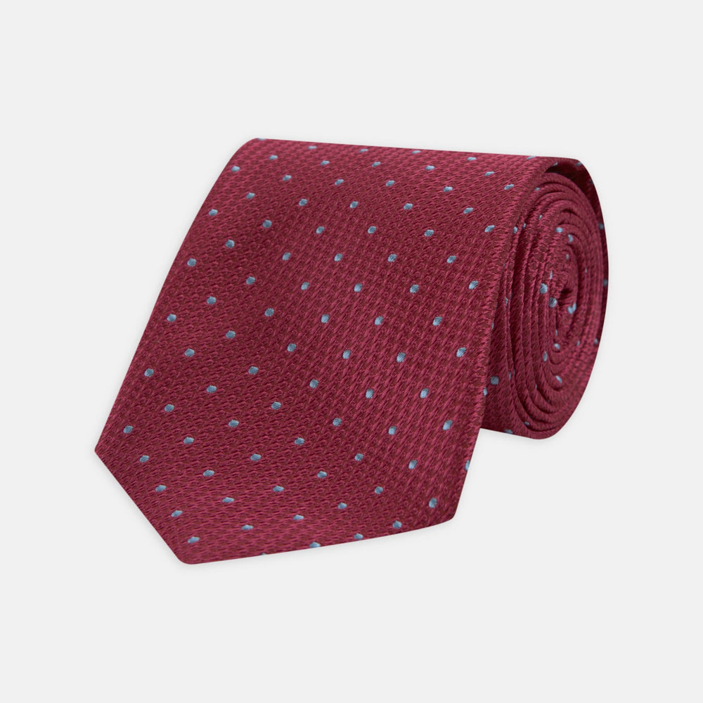 The Turnbull & Asser Dark Pink and Blue Spot Lace Silk Tie features small, evenly spaced blue dots on dark pink silk, shown rolled up against a white background.