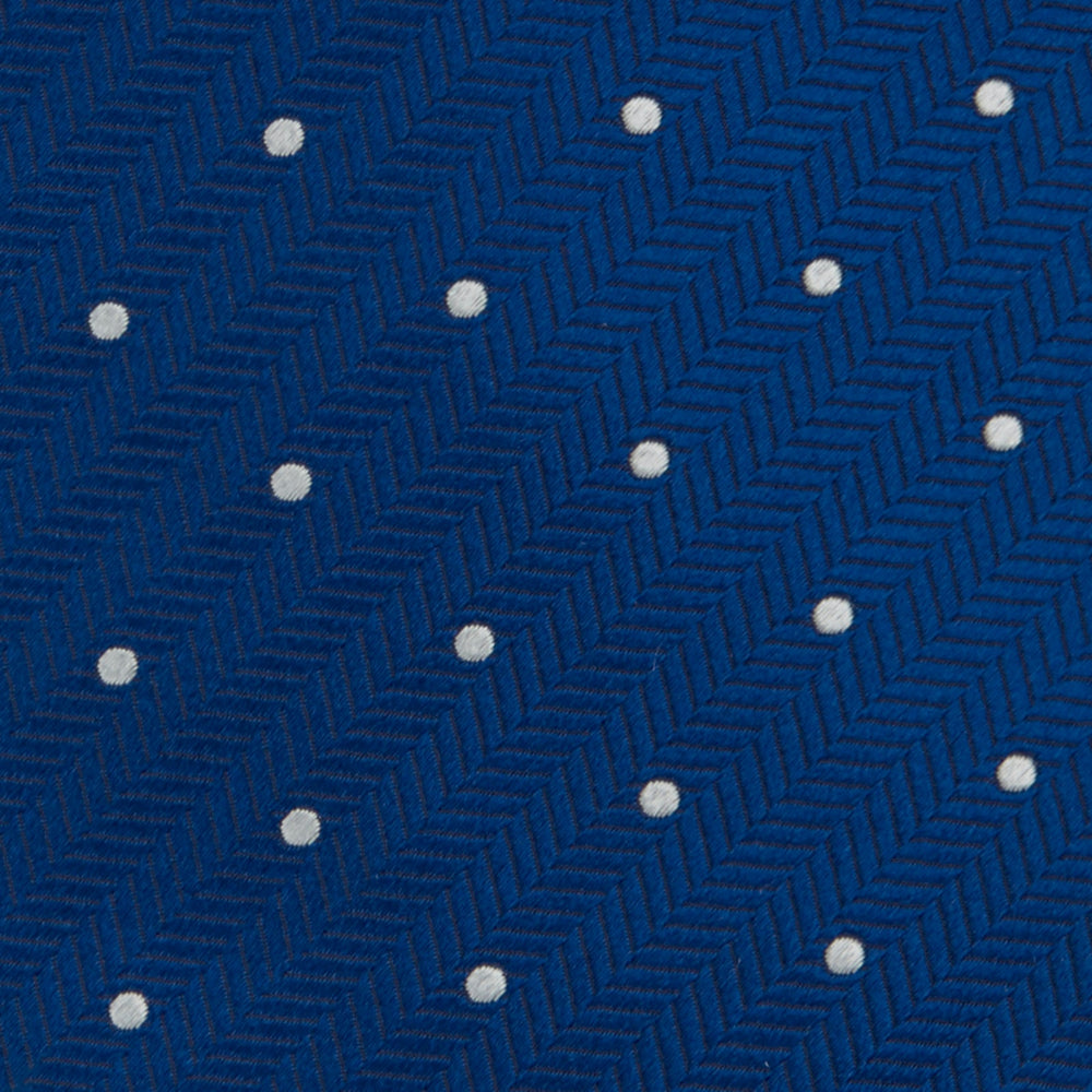 The Turnbull & Asser Royal Blue and White Small Spot Herringbone Silk Tie is displayed rolled at one end on a plain white background, showcasing its classic English silk design with subtle white polka dots.