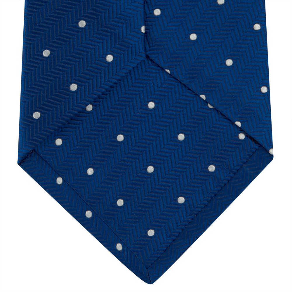 The Turnbull & Asser Royal Blue and White Small Spot Herringbone Silk Tie is displayed rolled at one end on a plain white background, showcasing its classic English silk design with subtle white polka dots.