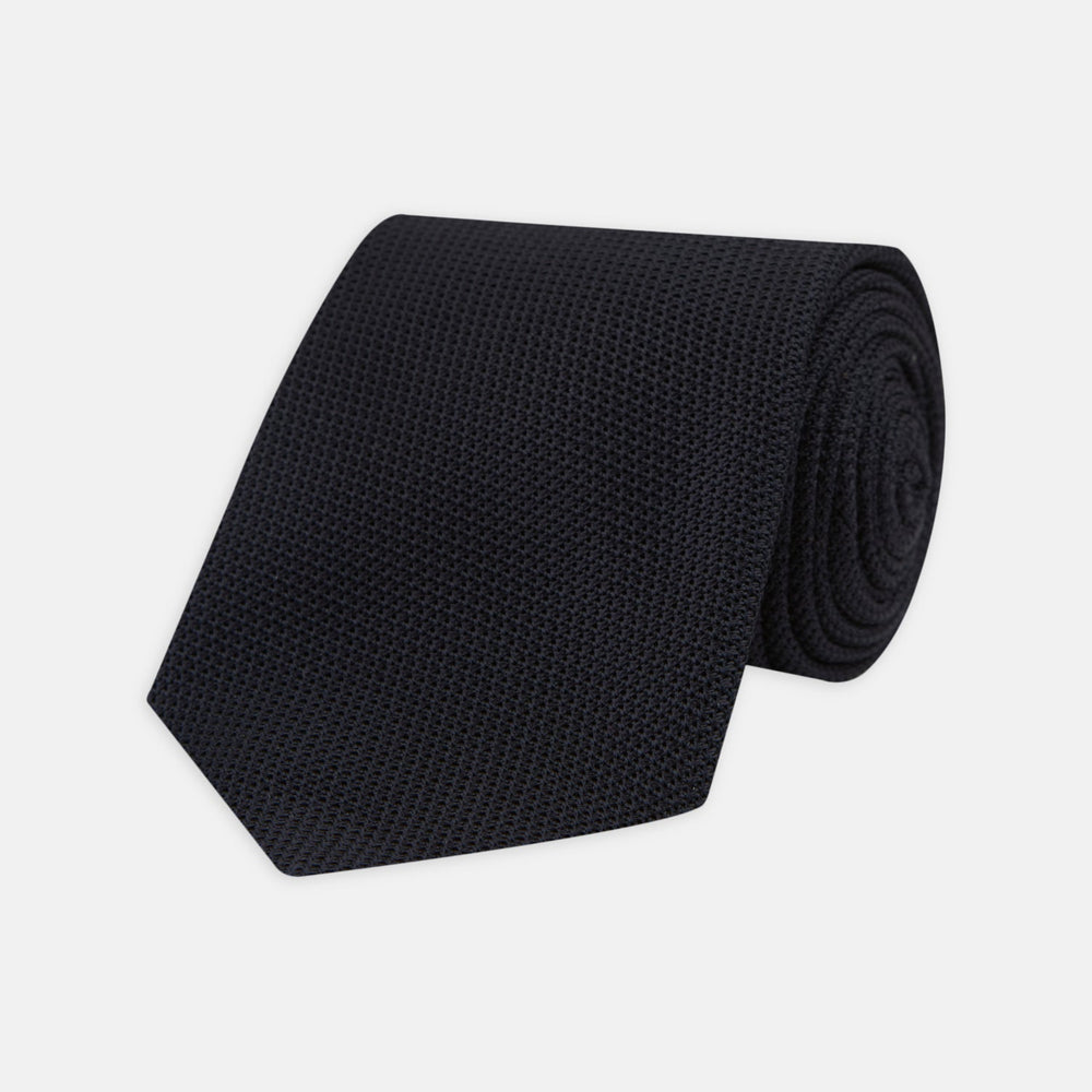A neatly rolled Turnbull & Asser Navy Grenadine Silk Tie with a textured, knitted appearance is displayed on a white background.