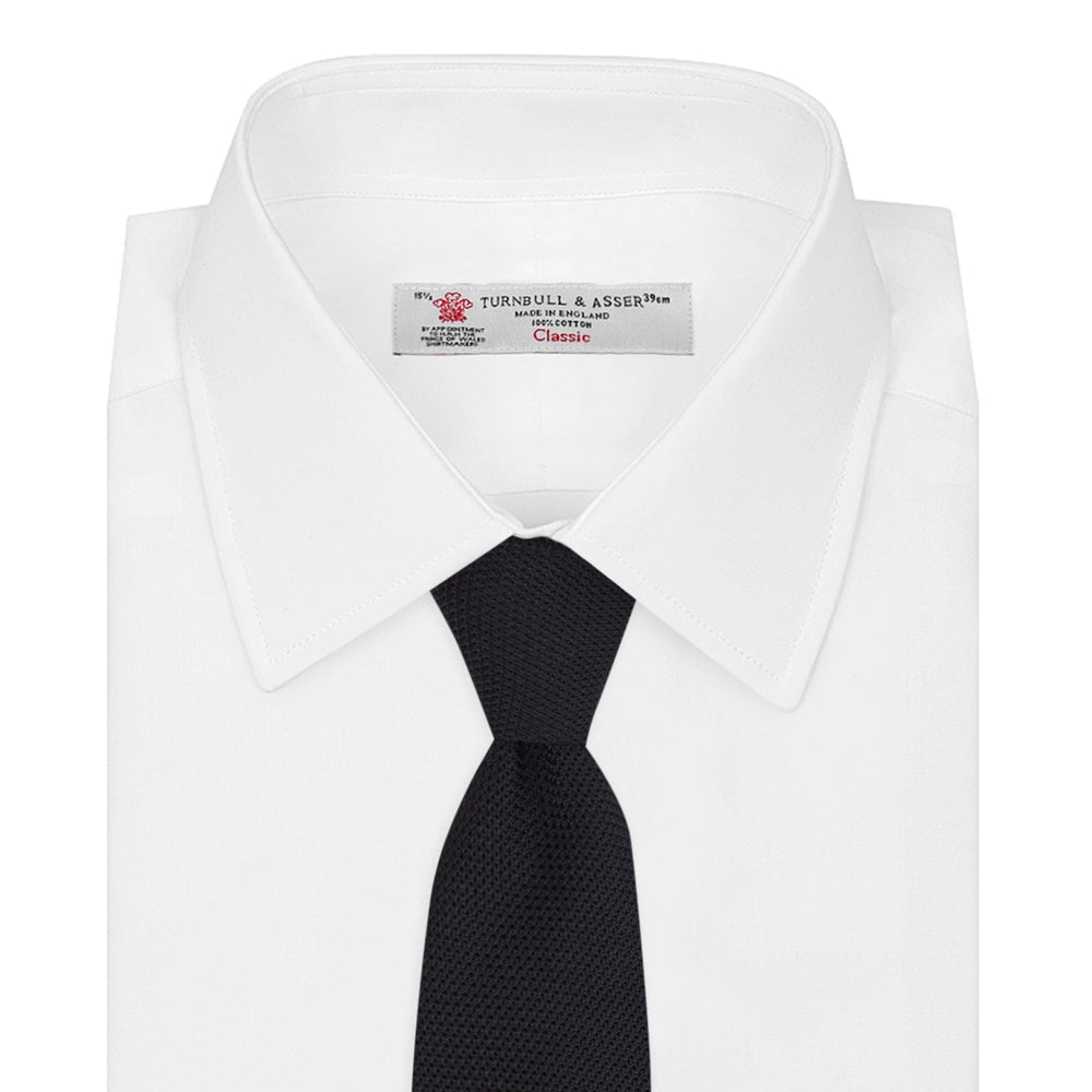A neatly rolled Turnbull & Asser Navy Grenadine Silk Tie with a textured, knitted appearance is displayed on a white background.