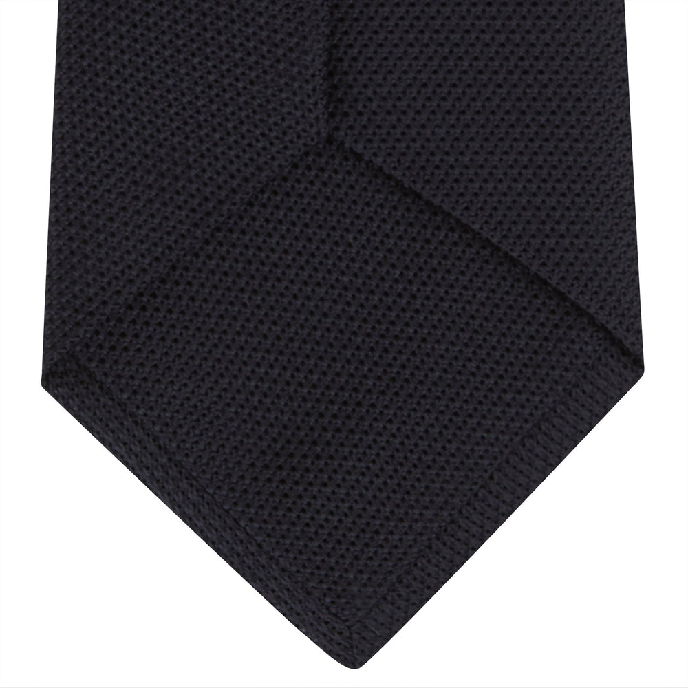 A neatly rolled Turnbull & Asser Navy Grenadine Silk Tie with a textured, knitted appearance is displayed on a white background.