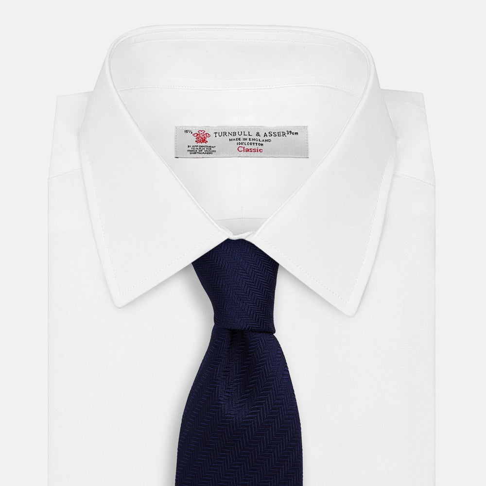 The Turnbull & Asser Slim Navy Herringbone Silk Tie is a refined men’s accessory, elegantly rolled and displayed on a plain white background.
