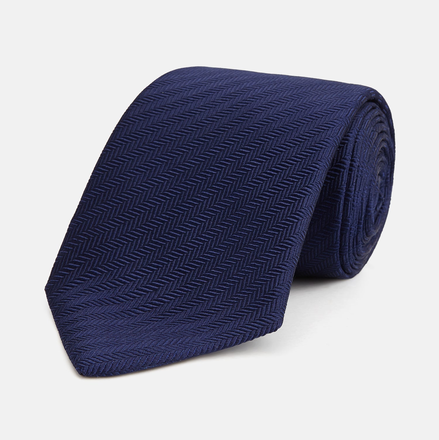 View 1 of product The Turnbull & Asser Slim Navy Herringbone Silk Tie is a refined men’s accessory, elegantly rolled and displayed on a plain white background.