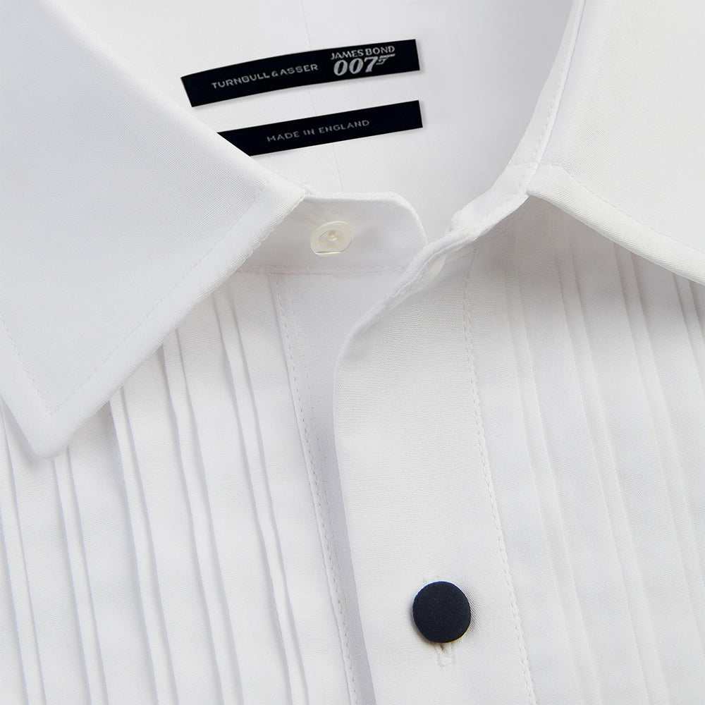 The Casino Royale White Dress Shirt in Cotton by Turnbull & Asser UK is a long-sleeve white dress shirt, crafted from crisp white cotton poplin with a pleated bib front, black buttons, and a classic collar, shown laid flat on a white background.