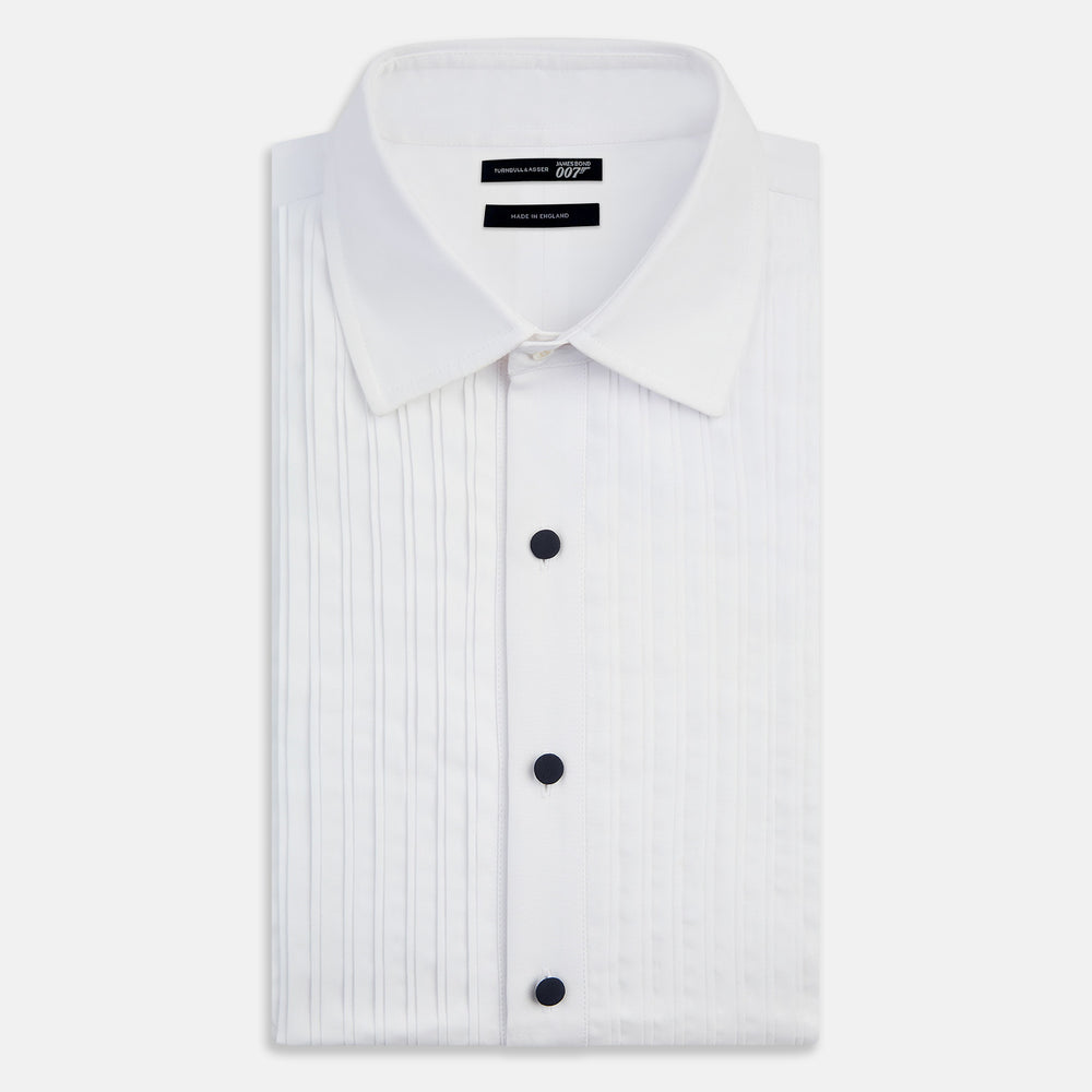 The Casino Royale White Dress Shirt in Cotton by Turnbull & Asser UK is a long-sleeve white dress shirt, crafted from crisp white cotton poplin with a pleated bib front, black buttons, and a classic collar, shown laid flat on a white background.