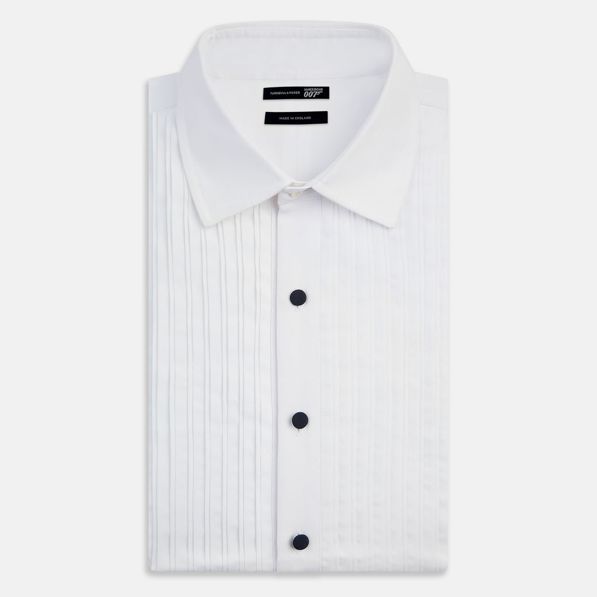 View 4 of product The Casino Royale White Dress Shirt in Cotton by Turnbull & Asser UK is a long-sleeve white dress shirt, crafted from crisp white cotton poplin with a pleated bib front, black buttons, and a classic collar, shown laid flat on a white background.
