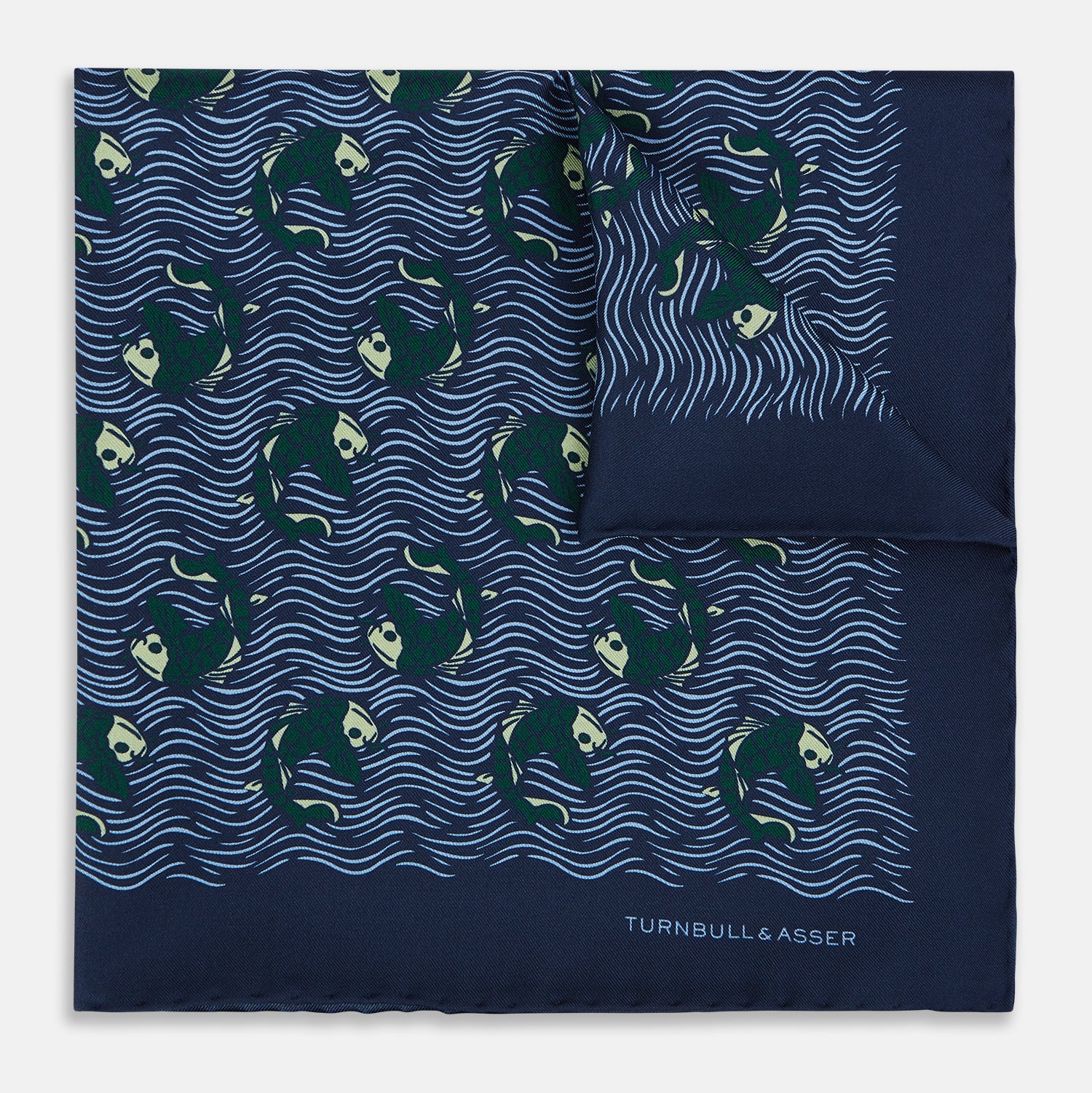 View 1 of product The Navy Blue Wave Silk Pocket Square by Turnbull & Asser UK showcases a playful motif of green and white fish swimming among wavy blue lines, with the brand’s name printed in white in the corner.