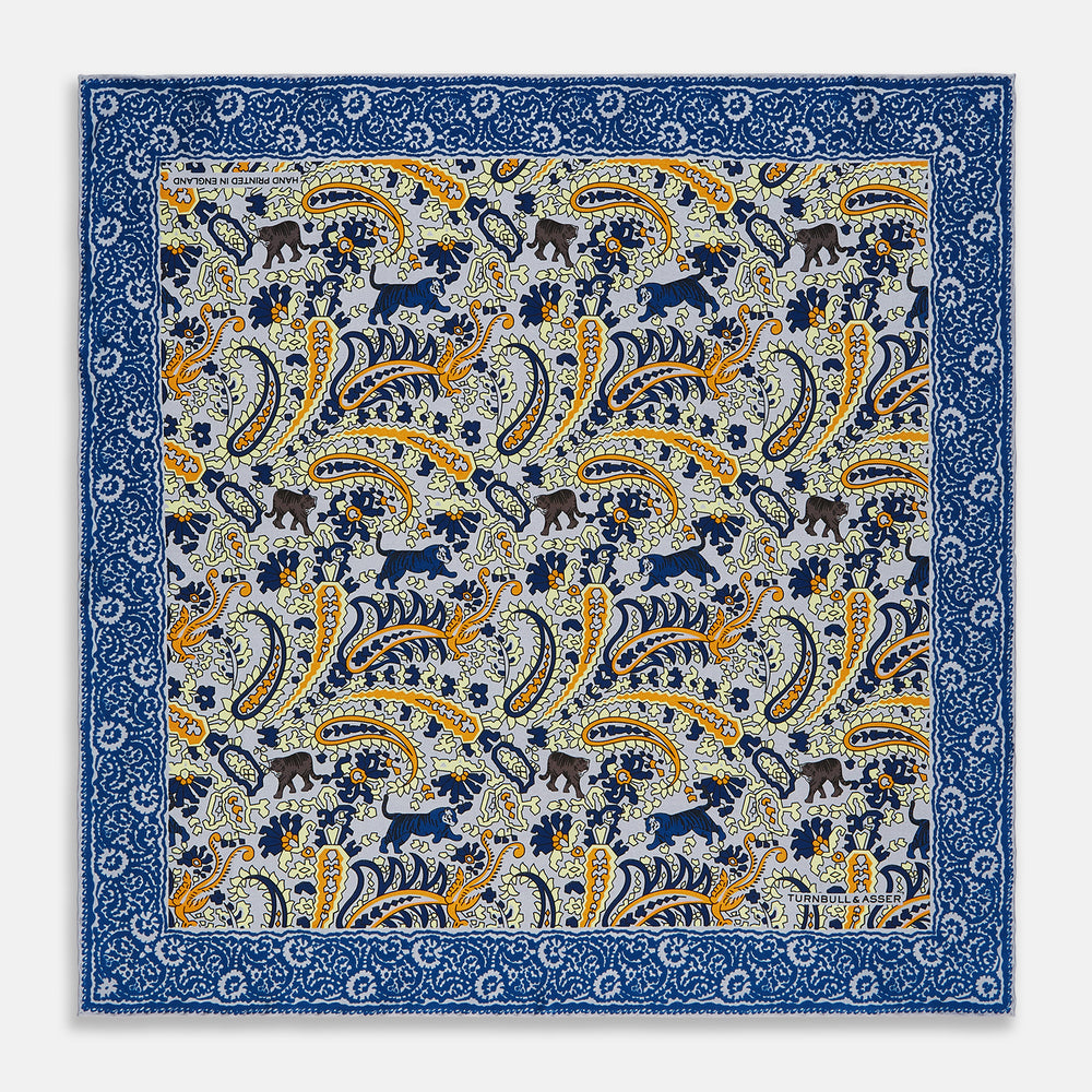 The Blue and Yellow Paisley Tiger Silk Pocket Square by Turnbull & Asser features a light blue base with paisley, elephants, tigers, and floral motifs—highlighted by a blue border. An elegant choice to pair with any Turnbull shirt.