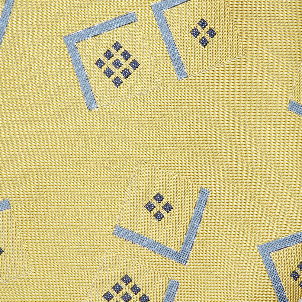 The Turnbull & Asser Yellow Graphic Deco Silk Tie features a subtle pattern of light blue geometric shapes and small black dots, elegantly rolled against a white background.