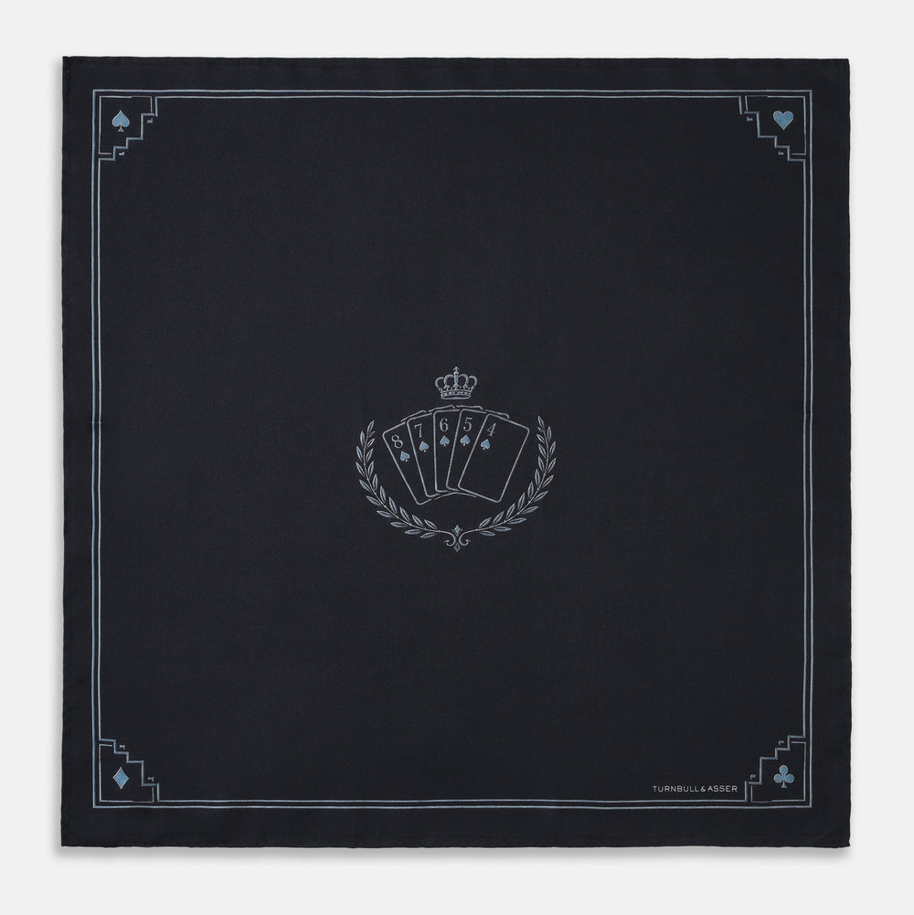 Introducing the Casino Royale Midnight Blue Crest Pocket Square in Silk from Turnbull & Asser UK—a midnight blue silk pocket square bordered in white, featuring playing card suit symbols at each corner and a central motif depicting the 10, J, Q, and K of spades beneath a crown and laurel. Perfect as a sophisticated Casino Royale or Bond tuxedo accessory, with “Turnbull & Asser” elegantly displayed in the lower right.