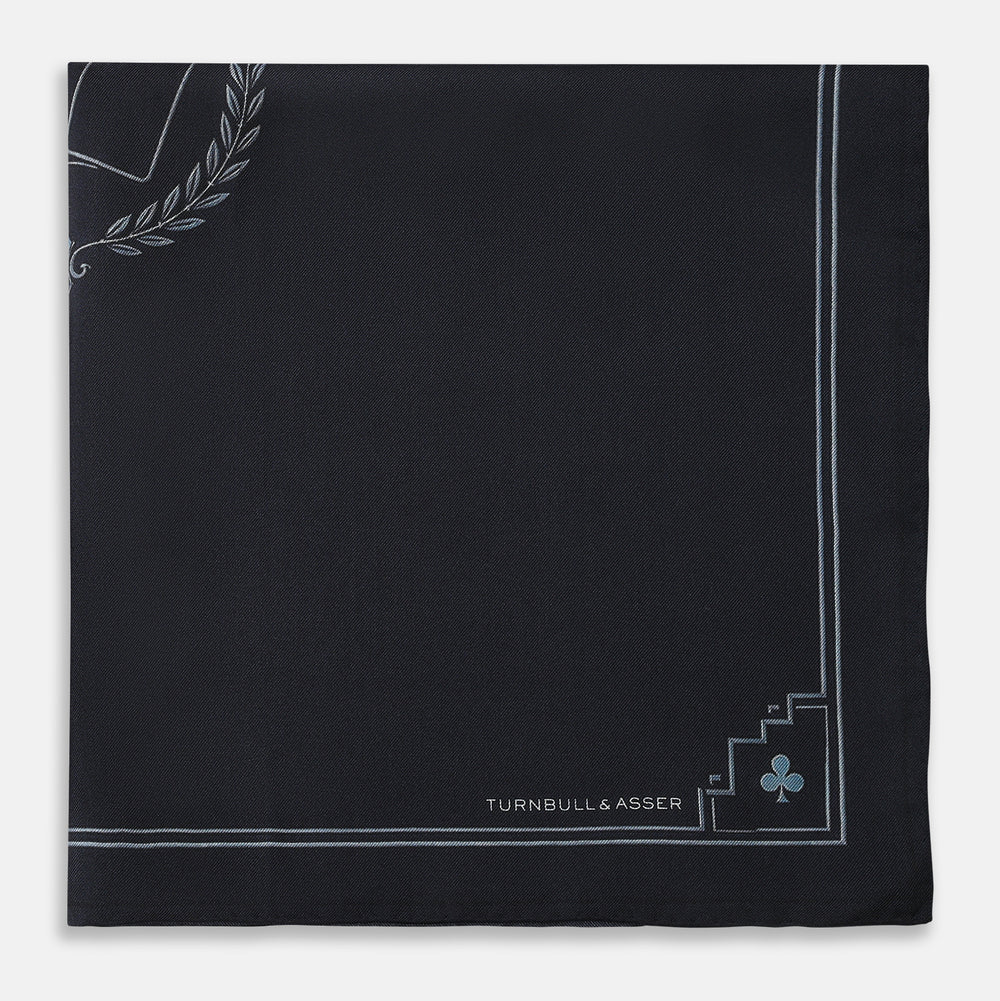 Introducing the Casino Royale Midnight Blue Crest Pocket Square in Silk from Turnbull & Asser UK—a midnight blue silk pocket square bordered in white, featuring playing card suit symbols at each corner and a central motif depicting the 10, J, Q, and K of spades beneath a crown and laurel. Perfect as a sophisticated Casino Royale or Bond tuxedo accessory, with “Turnbull & Asser” elegantly displayed in the lower right.