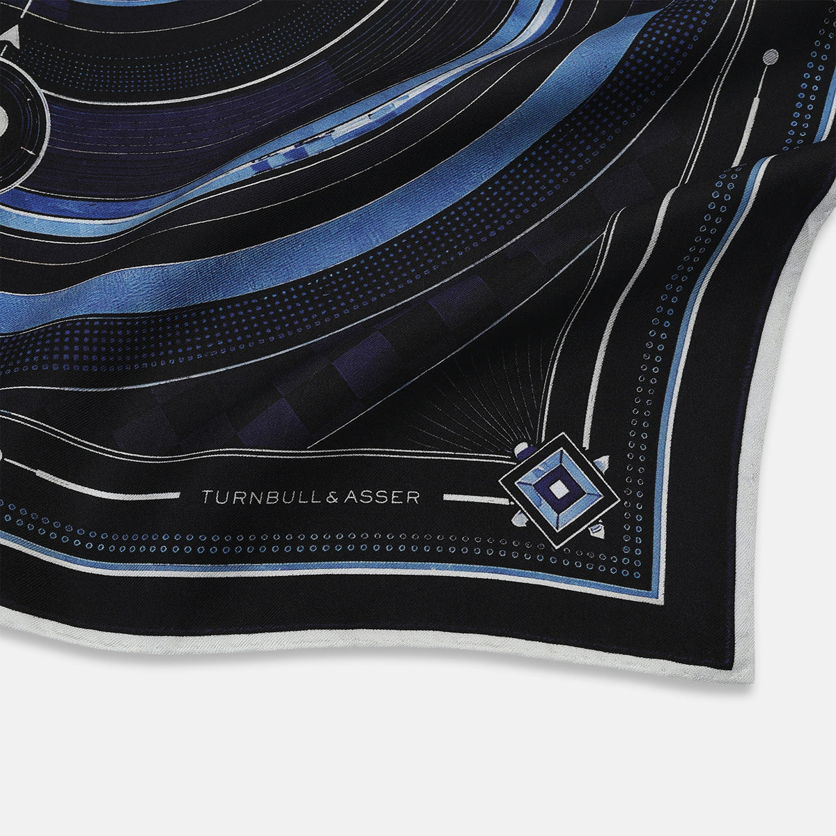 View 2 of product Presenting the Casino Royale Midnight Blue Target Pocket Square in Silk from Turnbull & Asser UK—a luxurious silk square scarf adorned with concentric circles in rich midnight blue and black, accented by playing card suit symbols (spade, diamond, club, heart) at each cardinal point and striking geometric patterns in the corners. This elegant accessory is perfect for adding a touch of sophisticated intrigue to your ensemble.