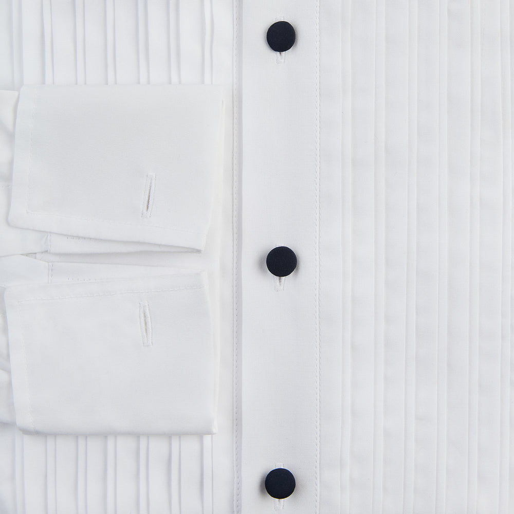 The Casino Royale White Dress Shirt in Cotton by Turnbull & Asser UK is a long-sleeve white dress shirt, crafted from crisp white cotton poplin with a pleated bib front, black buttons, and a classic collar, shown laid flat on a white background.