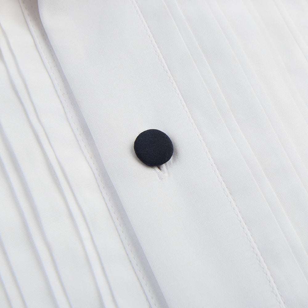 The Casino Royale White Dress Shirt in Cotton by Turnbull & Asser UK is a long-sleeve white dress shirt, crafted from crisp white cotton poplin with a pleated bib front, black buttons, and a classic collar, shown laid flat on a white background.