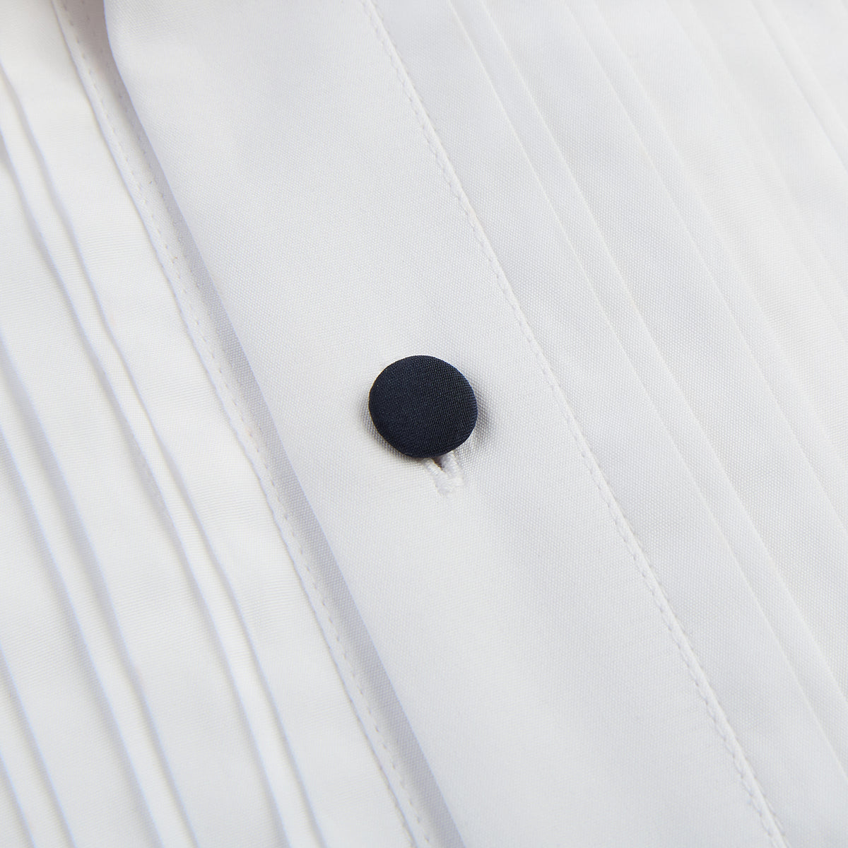 View 7 of product The Casino Royale White Dress Shirt in Cotton by Turnbull & Asser UK is a long-sleeve white dress shirt, crafted from crisp white cotton poplin with a pleated bib front, black buttons, and a classic collar, shown laid flat on a white background.