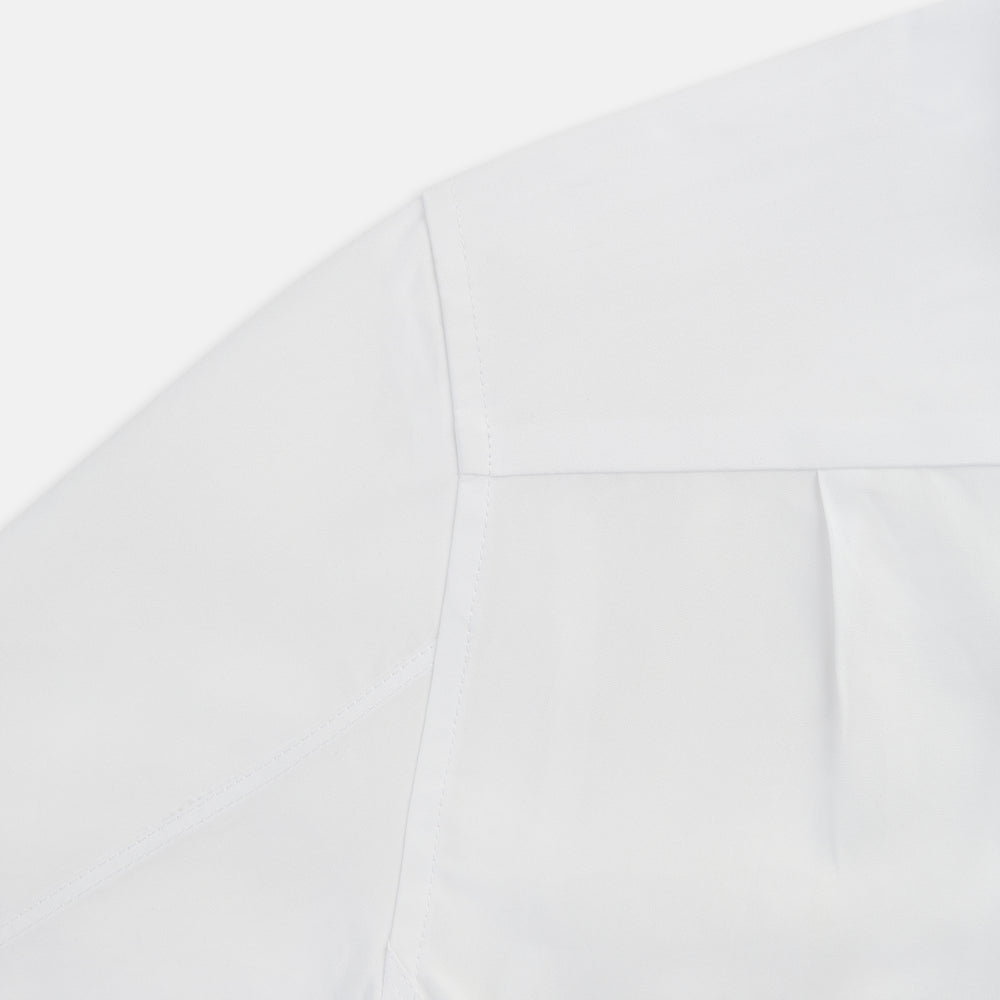 The Casino Royale White Dress Shirt in Cotton by Turnbull & Asser UK is a long-sleeve white dress shirt, crafted from crisp white cotton poplin with a pleated bib front, black buttons, and a classic collar, shown laid flat on a white background.