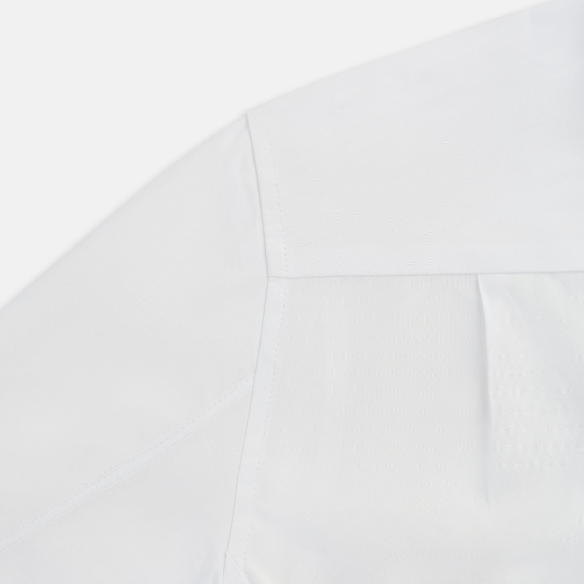 View 5 of product The Casino Royale White Dress Shirt in Cotton by Turnbull & Asser UK is a long-sleeve white dress shirt, crafted from crisp white cotton poplin with a pleated bib front, black buttons, and a classic collar, shown laid flat on a white background.