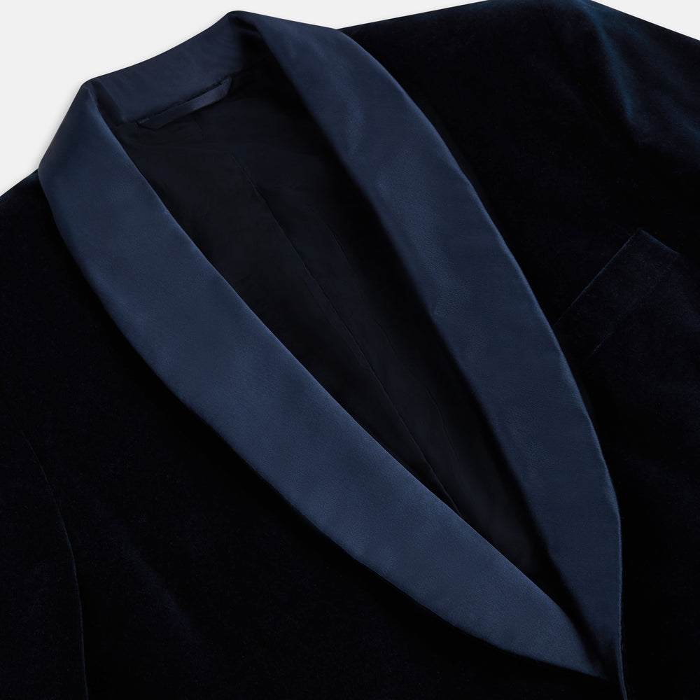 Turnbull & Asser UK’s Casino Royale Midnight Blue Tuxedo Jacket in Cotton Velvet, featuring a single button closure and a luxurious silk-satin shawl lapel, is showcased against a plain white background.