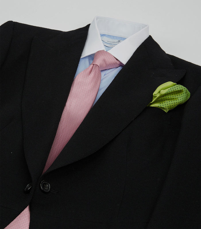 A black suit jacket with a light blue shirt, pink tie, and green polka-dotted pocket square arranged on a flat surface, as if worn on an invisible person.