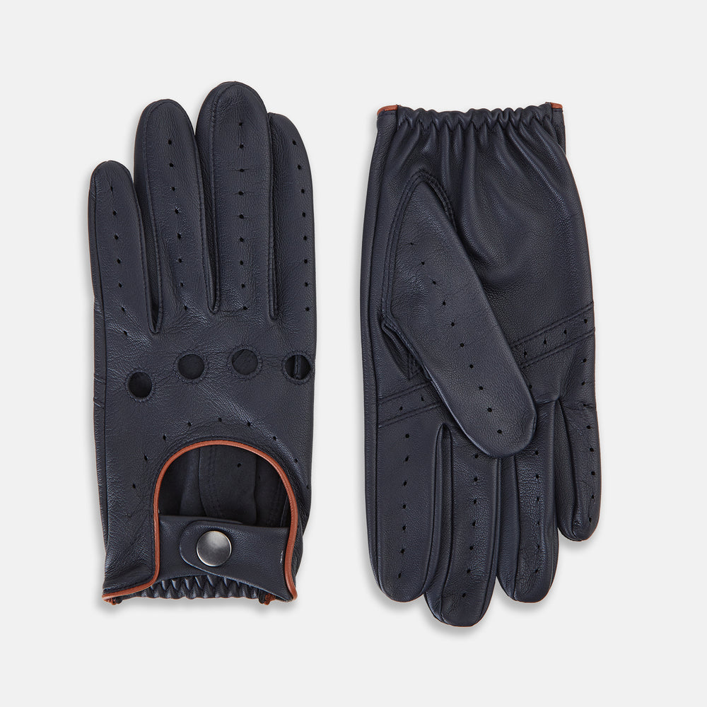 A pair of navy leather driving gloves from Turnbull & Asser UK, featuring perforations and snap closures; one glove displays the palm side while the other shows the back. These unlined Navy Driving Gloves combine style and flexibility for an optimal driving experience.