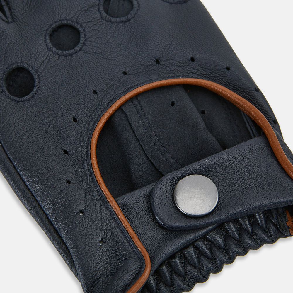 A pair of navy leather driving gloves from Turnbull & Asser UK, featuring perforations and snap closures; one glove displays the palm side while the other shows the back. These unlined Navy Driving Gloves combine style and flexibility for an optimal driving experience.