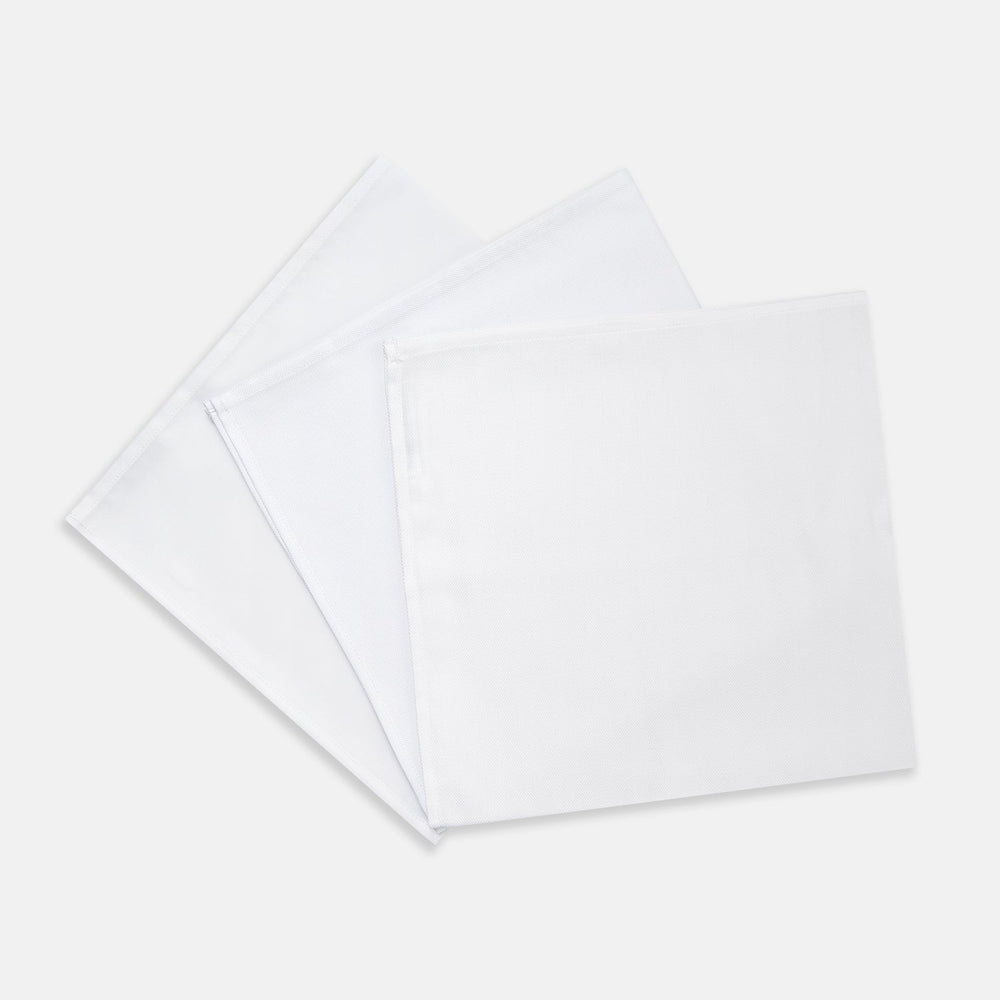Three Turnbull & Asser Plain White Cotton Handkerchiefs from the 3-pack are neatly folded and overlapping on a light gray background.