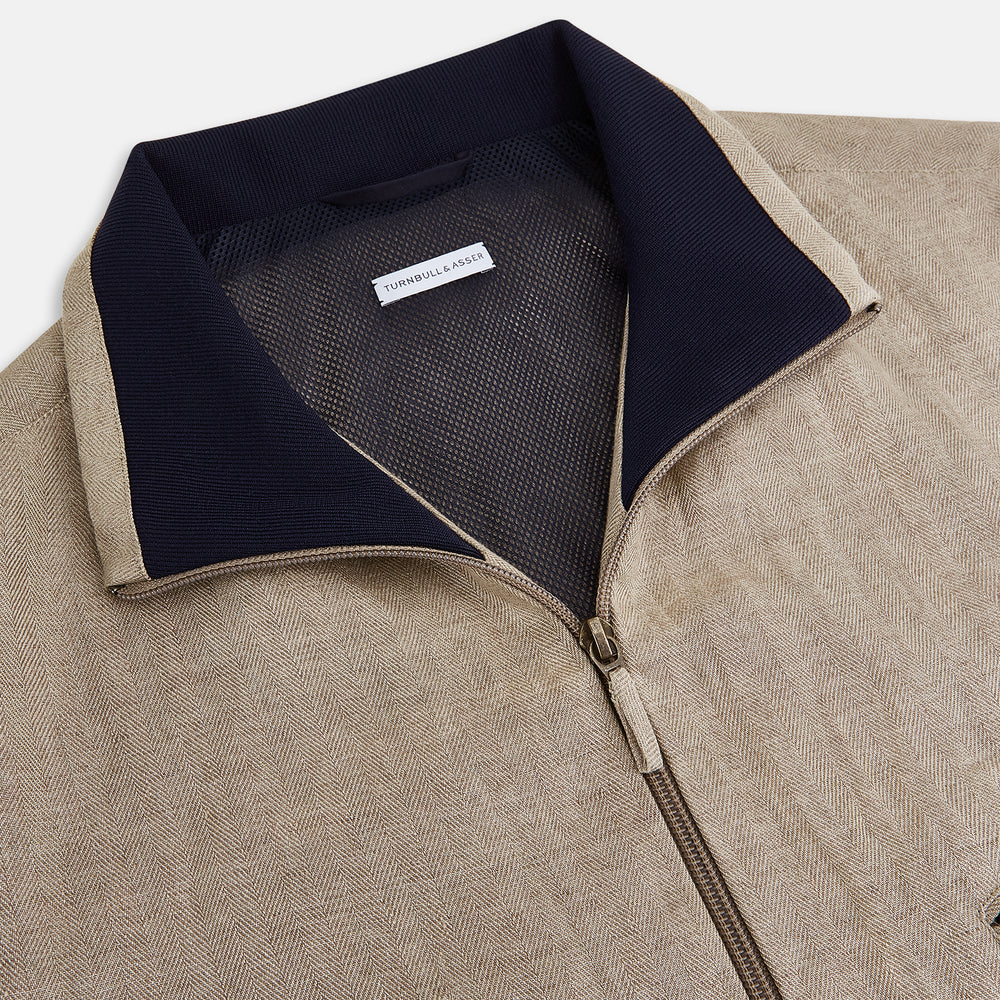 A Fairway Sand Golf Jacket in Linen by Turnbull & Asser UK, crafted from lightweight herringbone linen, features a front zipper, a chest zip pocket, two side zip pockets, and dark navy cuffs, collar lining, and waistband. Shown on a plain white background.