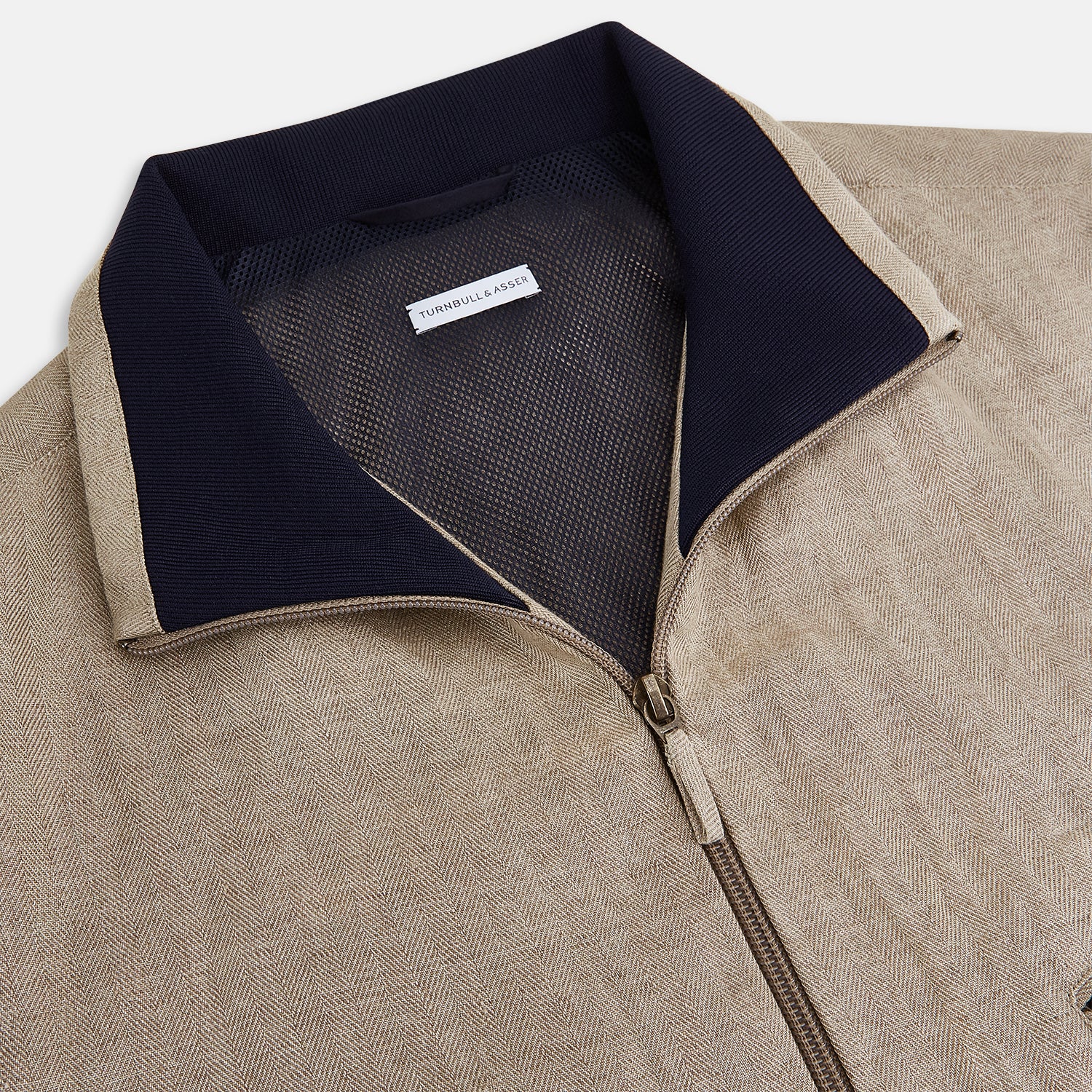 View 2 of product A Fairway Sand Golf Jacket in Linen by Turnbull & Asser UK, crafted from lightweight herringbone linen, features a front zipper, a chest zip pocket, two side zip pockets, and dark navy cuffs, collar lining, and waistband. Shown on a plain white background.