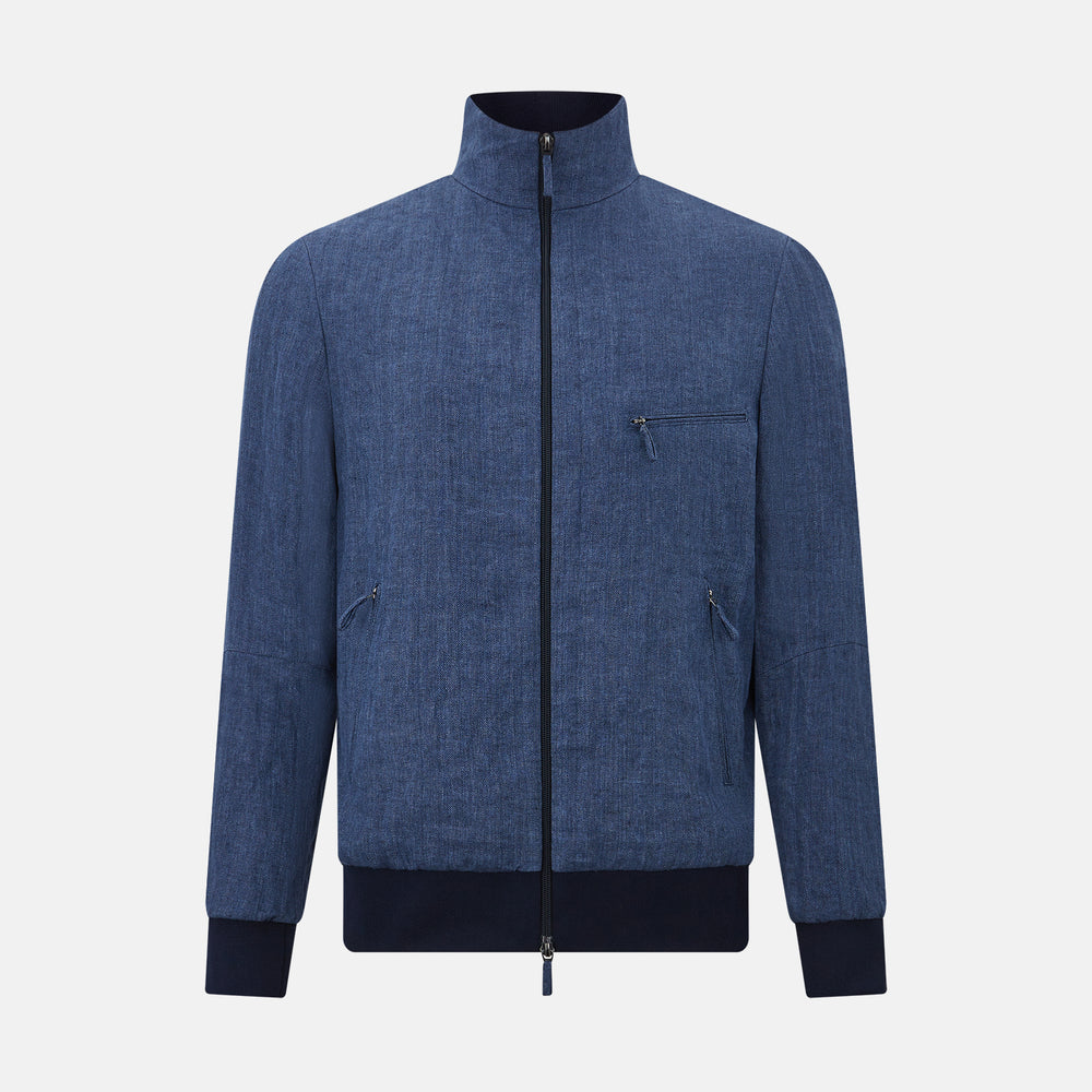 Introducing the Fairway Denim Golf Jacket in Linen by Turnbull & Asser UK—a blue zip-up jacket featuring a high collar, two side pockets, and a zippered chest pocket. The contrasting darker cuffs and hem accentuate its denim-like linen texture, making it the perfect versatile golf jacket for cooler days.