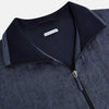 View 2 of product Introducing the Fairway Denim Golf Jacket in Linen by Turnbull & Asser UK—a blue zip-up jacket featuring a high collar, two side pockets, and a zippered chest pocket. The contrasting darker cuffs and hem accentuate its denim-like linen texture, making it the perfect versatile golf jacket for cooler days.