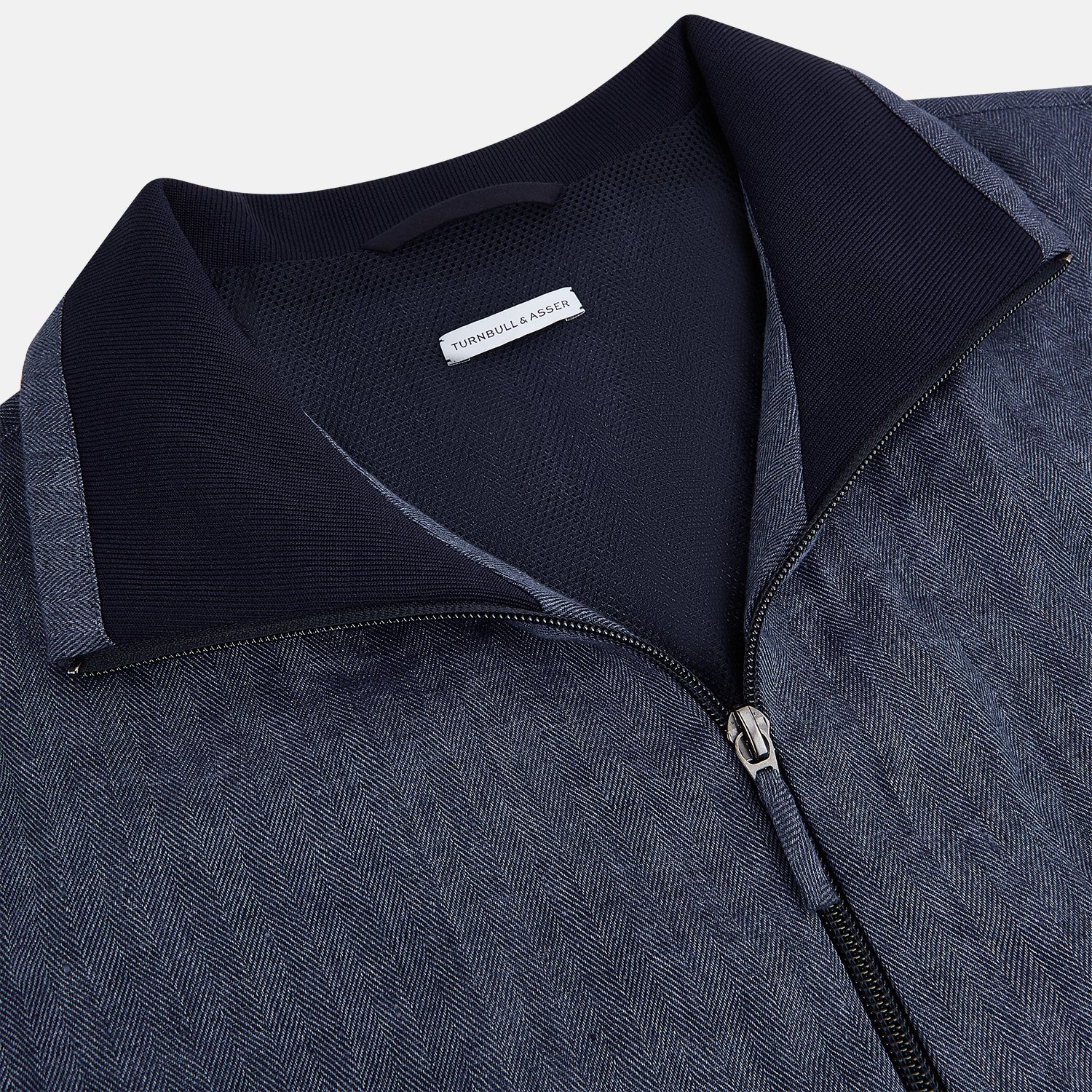 View 2 of product Introducing the Fairway Denim Golf Jacket in Linen by Turnbull & Asser UK—a blue zip-up jacket featuring a high collar, two side pockets, and a zippered chest pocket. The contrasting darker cuffs and hem accentuate its denim-like linen texture, making it the perfect versatile golf jacket for cooler days.