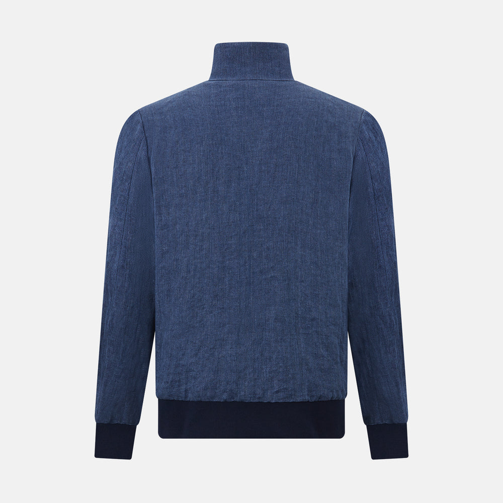 Introducing the Fairway Denim Golf Jacket in Linen by Turnbull & Asser UK—a blue zip-up jacket featuring a high collar, two side pockets, and a zippered chest pocket. The contrasting darker cuffs and hem accentuate its denim-like linen texture, making it the perfect versatile golf jacket for cooler days.