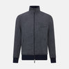 View 1 of product A front view of the Fairway Ash Golf Jacket in Linen by Turnbull & Asser UK is shown, featuring a high collar, two side zip pockets, a chest zip pocket, and black ribbed cuffs and hem. Crafted from lightweight gray herringbone linen for effortless warm-weather dressing, the jacket is displayed on a plain white background.