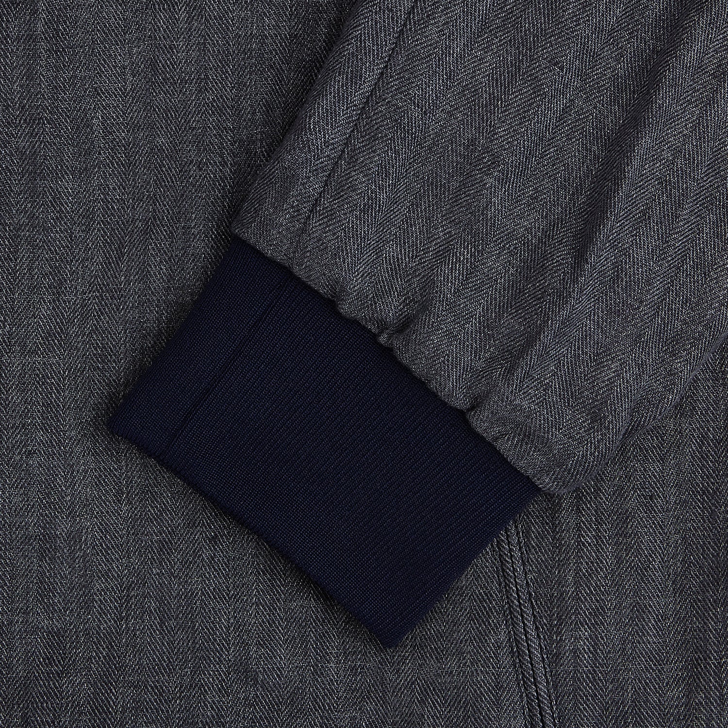 View 4 of product A front view of the Fairway Ash Golf Jacket in Linen by Turnbull & Asser UK is shown, featuring a high collar, two side zip pockets, a chest zip pocket, and black ribbed cuffs and hem. Crafted from lightweight gray herringbone linen for effortless warm-weather dressing, the jacket is displayed on a plain white background.