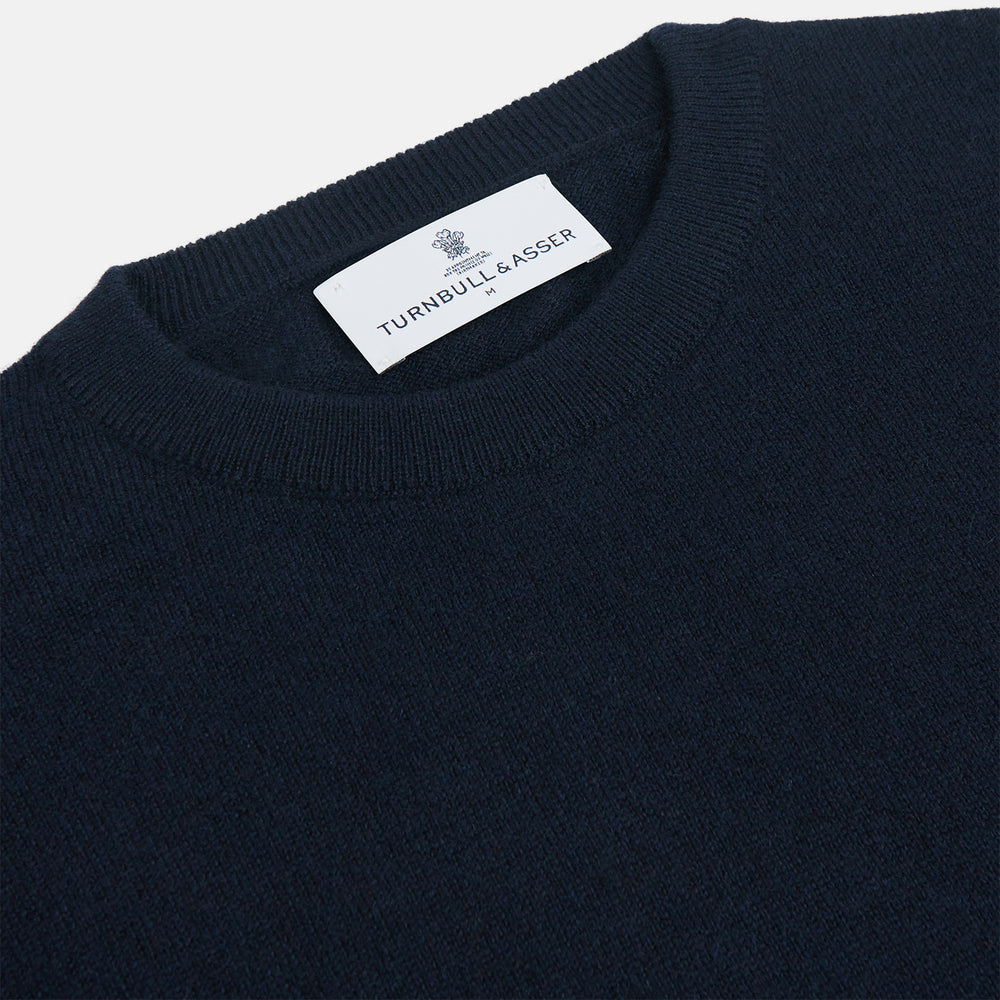 A luxurious navy crew neck cashmere jumper by Turnbull & Asser is laid flat on a white background, evoking timeless Scottish cashmere craftsmanship.
