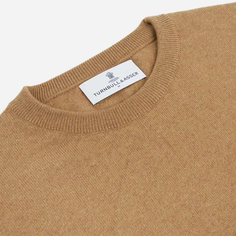 The Turnbull & Asser Camel Crew Neck Merino Wool Jumper is a classic, long-sleeve sweater in camel, laid flat on a white background. Featuring ribbed collar, cuffs, and hem, it’s an essential staple for every gentleman’s wardrobe.