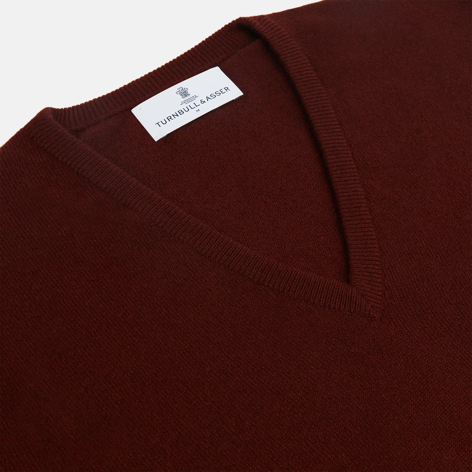 View 2 of product The Turnbull & Asser Port Cashmere V-Neck Jumper is a plain, long-sleeved burgundy sweater with a V-neck, shown flat on a white background.