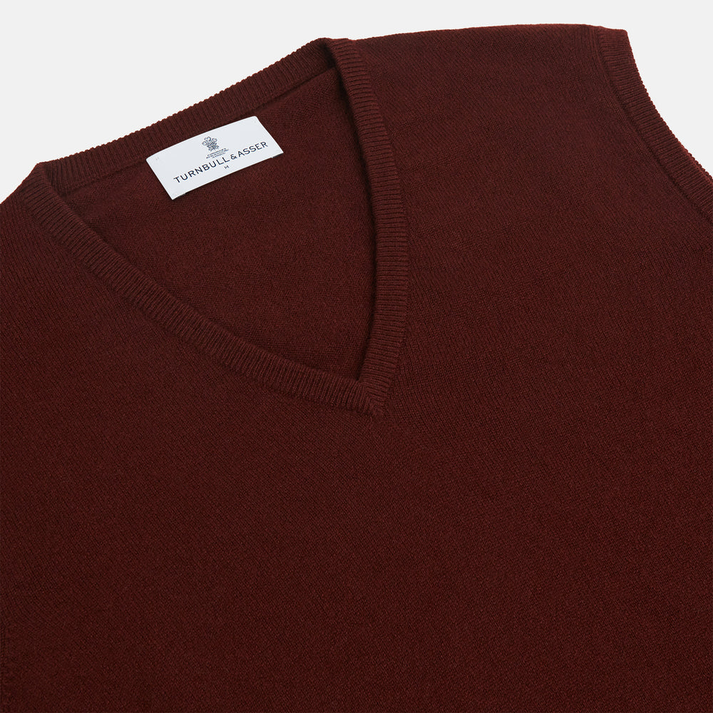 The Turnbull & Asser Port V-Neck Cashmere Slipover is a sleeveless, dark maroon vest with a simple design, shown laid flat on a white background—ideal for layering over a shirt or under a suit jacket.