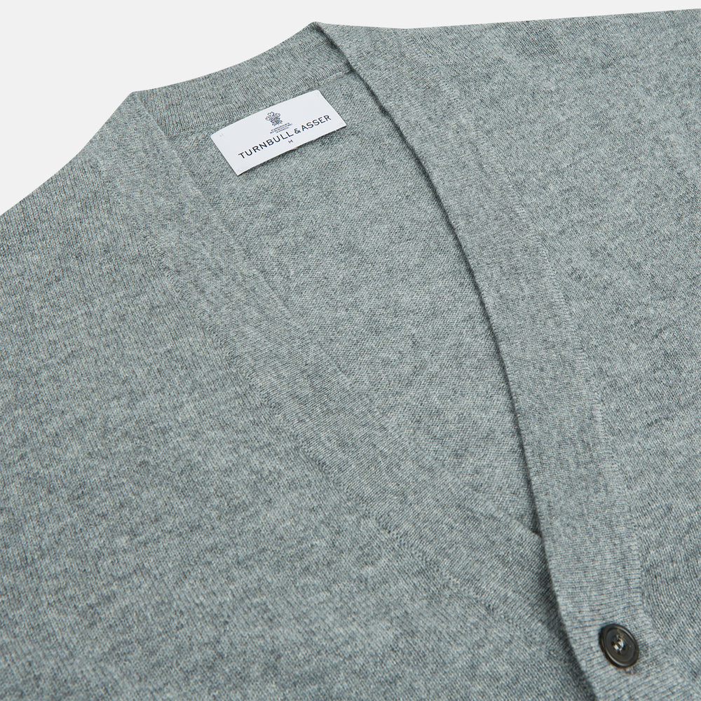 The Louis Flannel Grey Cashmere Cardigan by Turnbull & Asser features long sleeves, a V-neck, black front buttons, and two front pockets, making it ideal for transitional seasons. Shown laid flat on a white background.