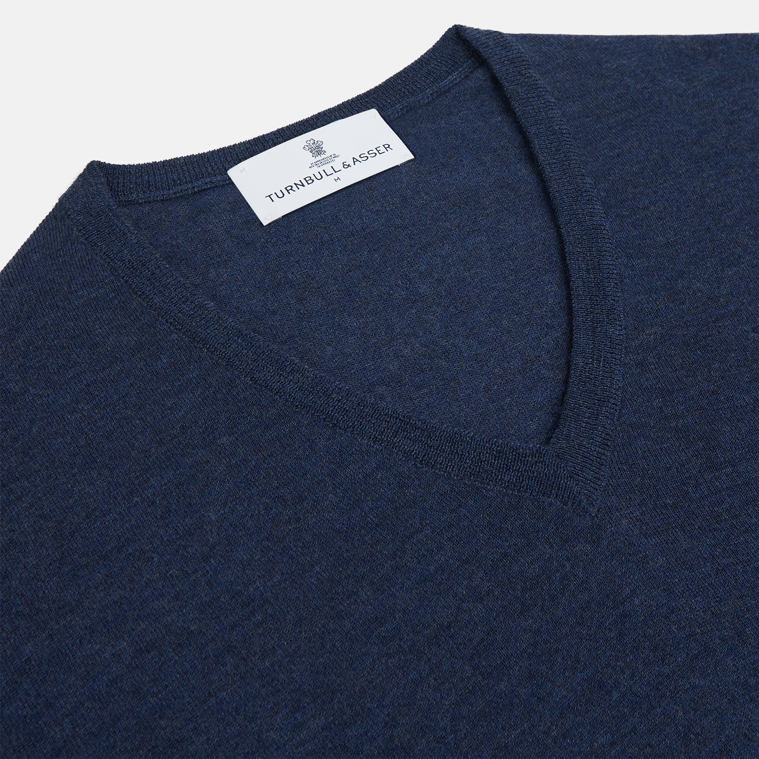 View 2 of product The Blue V-Neck Merino Wool Jumper by Turnbull & Asser features long sleeves, ribbed cuffs, and a ribbed hem—a timeless essential for any gentleman's wardrobe, shown laid flat on a white background.