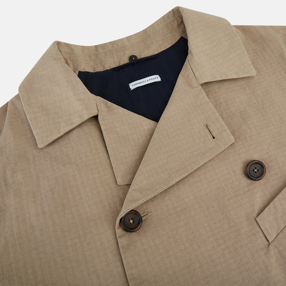 The Sand Long Albert Trench Coat by Turnbull & Asser UK features a double-breasted design, dark buttons, notched collar, and two slanted front pockets, offering timeless British style. Shown against a plain white background.