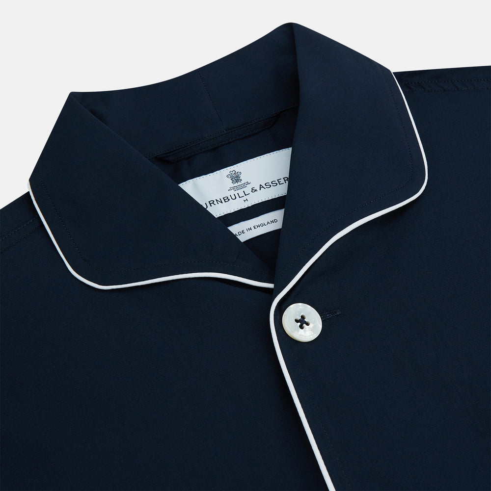 The Turnbull & Asser Navy Piped Cotton Pyjama Set features a navy blue long-sleeve top with white piping, front buttons, a chest pocket, and matching drawstring pants, all displayed on a white background.