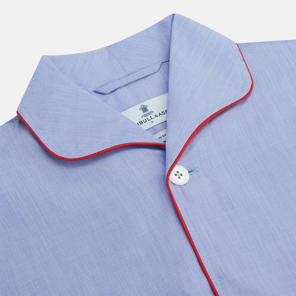 The Blue Piped End-on-End Cotton Pyjama Set by Turnbull & Asser features light blue long sleeves, red piping, front buttons, chest pocket, and matching drawstring pants—luxurious sleepwear laid flat on a white background.