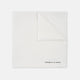 The White Piped Silk Pocket Square by Turnbull & Asser is shown folded at one corner with the brand's logo in black on the lower right, set against a light blue background.