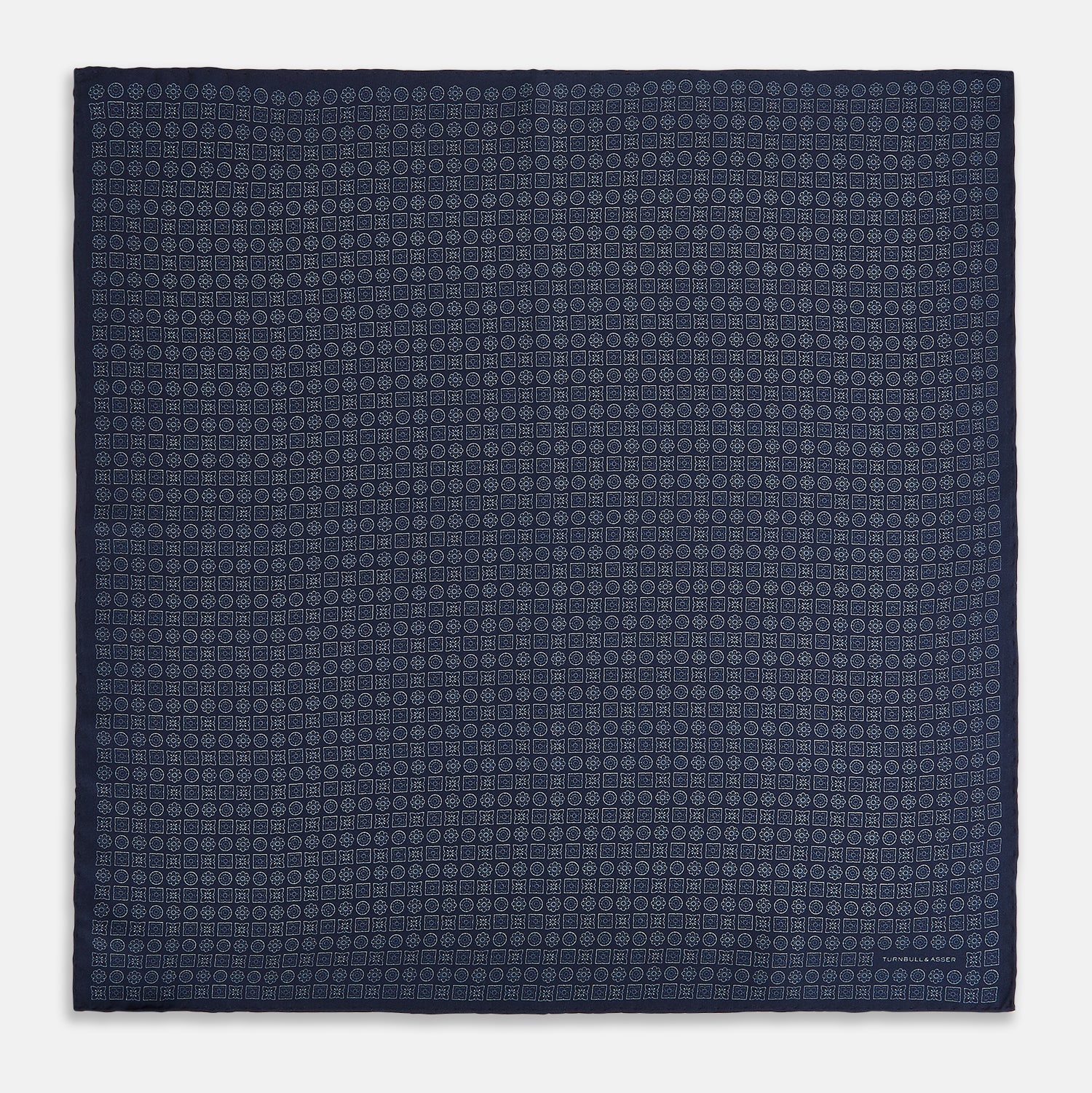 View 4 of product A Floral Navy Pocket Square in Silk by Turnbull & Asser UK, featuring a repeating geometric pattern with the brand’s name printed in white in the corner—perfect for adding a touch of sophistication to formal tailoring. The top right edge is folded over to reveal the reverse side.